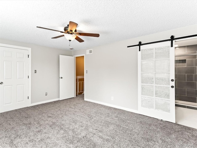 empty room with a barn door, visible vents, a ceiling fan, a textured ceiling, and carpet flooring