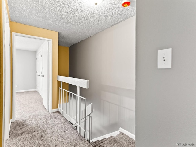 hallway with a textured ceiling, carpet floors, an upstairs landing, and baseboards