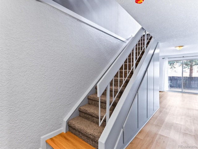 stairs featuring a textured wall, a textured ceiling, and wood finished floors