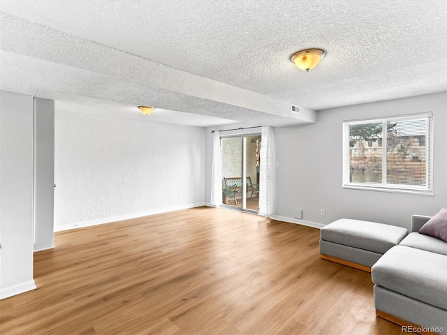 living room with visible vents, light wood-style flooring, baseboards, and a textured ceiling