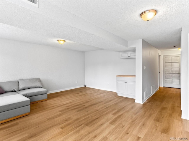 living room with baseboards, a textured ceiling, and light wood-style floors