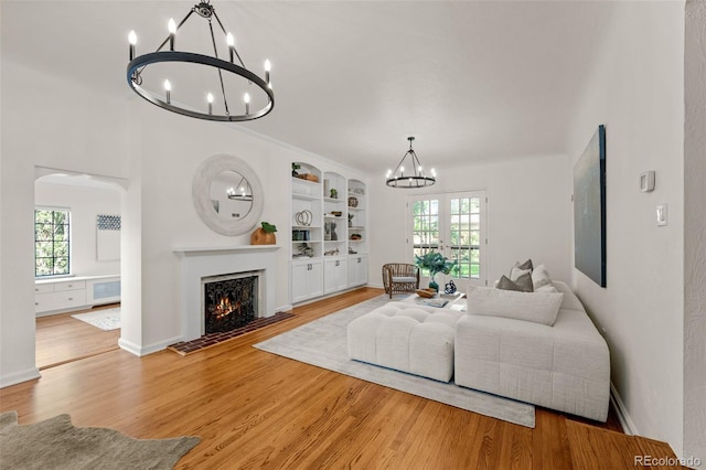 living room featuring light hardwood / wood-style flooring, built in features, a chandelier, and plenty of natural light