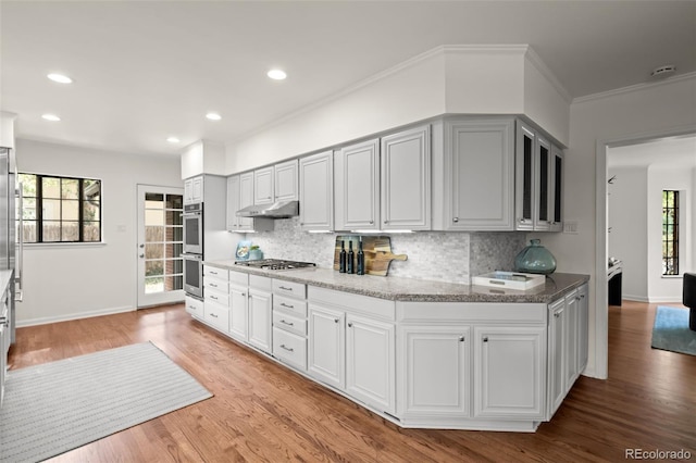 kitchen featuring stainless steel appliances, light stone countertops, light hardwood / wood-style floors, and backsplash