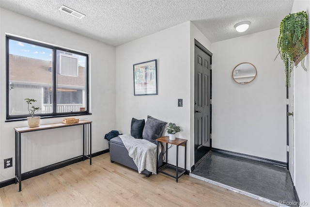 living area with a textured ceiling, baseboards, visible vents, and light wood-style floors