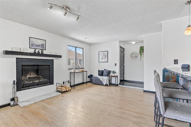 living room with a textured ceiling, baseboards, light wood-type flooring, and a fireplace with raised hearth