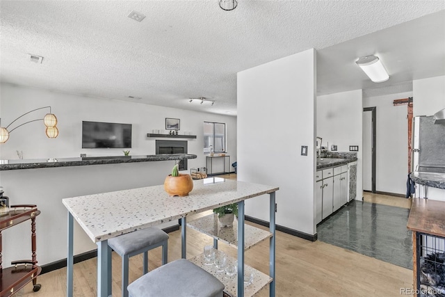kitchen featuring light wood-type flooring, a textured ceiling, baseboards, and dark countertops