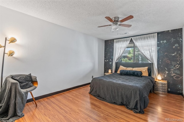 bedroom with wallpapered walls, a textured ceiling, visible vents, and wood finished floors
