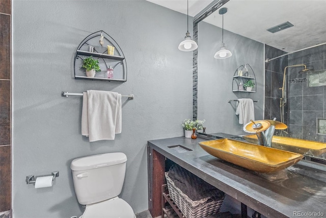 bathroom with toilet, a tile shower, vanity, and visible vents