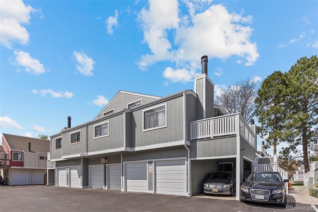rear view of property with a garage, a chimney, and driveway