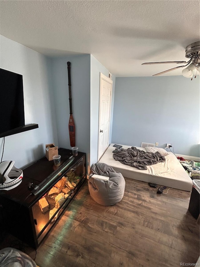 bedroom with a textured ceiling, ceiling fan, and dark wood-type flooring