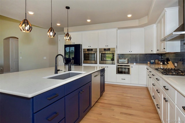 kitchen with blue cabinetry, sink, appliances with stainless steel finishes, wall chimney range hood, and white cabinets