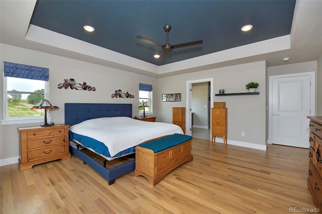 bedroom featuring light hardwood / wood-style flooring, a raised ceiling, and ceiling fan