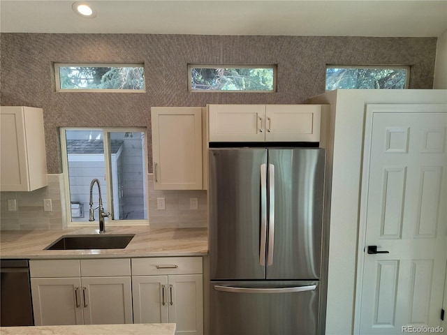 kitchen with appliances with stainless steel finishes, a sink, white cabinetry, decorative backsplash, and healthy amount of natural light
