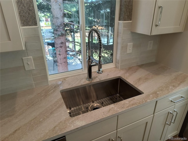 kitchen view of a sink, white cabinets, light stone countertops, and tasteful backsplash