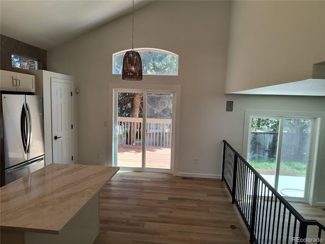 doorway featuring high vaulted ceiling, wood finished floors, healthy amount of natural light, and baseboards