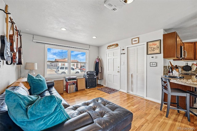 living room with recessed lighting, baseboards, a textured ceiling, and light wood-style flooring