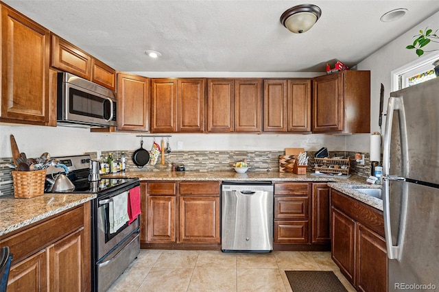 kitchen featuring light stone counters, light tile patterned floors, brown cabinets, and appliances with stainless steel finishes