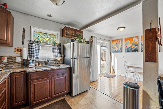 kitchen with light tile patterned floors, freestanding refrigerator, a sink, a textured ceiling, and backsplash