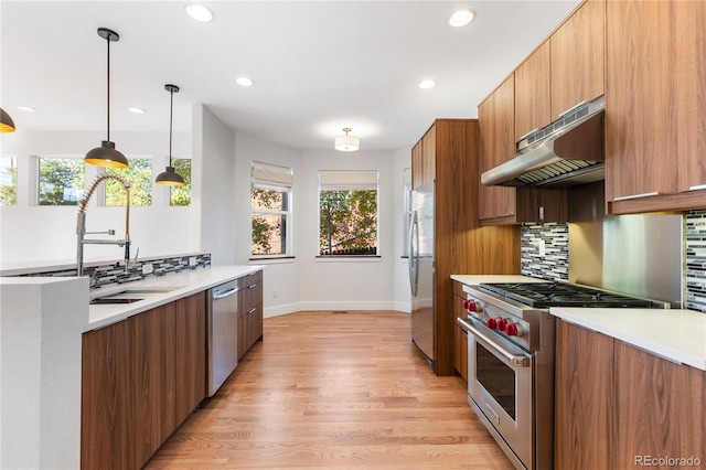 kitchen featuring tasteful backsplash, range hood, hanging light fixtures, light hardwood / wood-style flooring, and stainless steel appliances