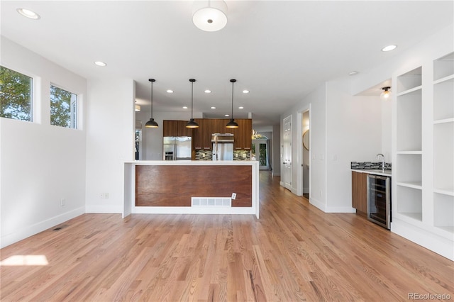 kitchen with stainless steel refrigerator with ice dispenser, hanging light fixtures, sink, light hardwood / wood-style floors, and beverage cooler