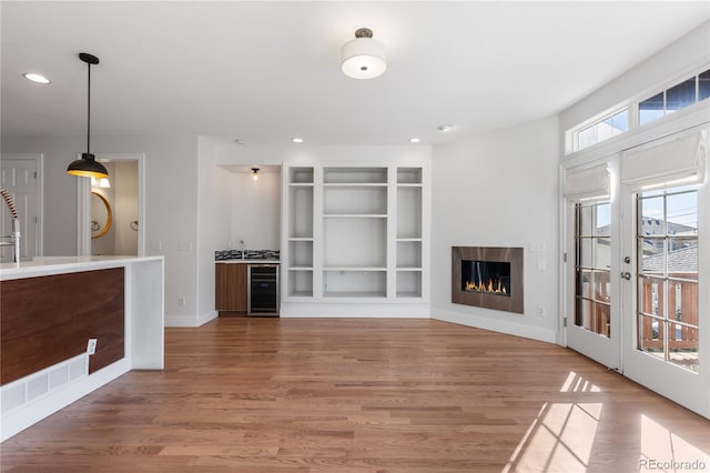 unfurnished living room with hardwood / wood-style flooring, built in shelves, and wine cooler