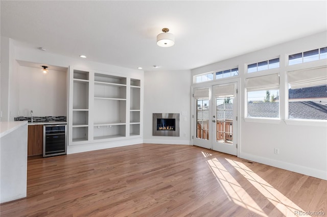 unfurnished living room featuring beverage cooler, french doors, sink, built in features, and hardwood / wood-style flooring