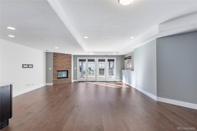 unfurnished living room with dark hardwood / wood-style floors, a tray ceiling, a stone fireplace, and french doors