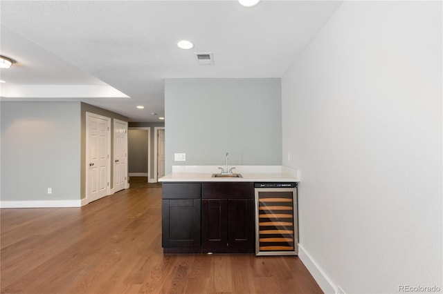 bar featuring sink, dark brown cabinets, light hardwood / wood-style flooring, and beverage cooler