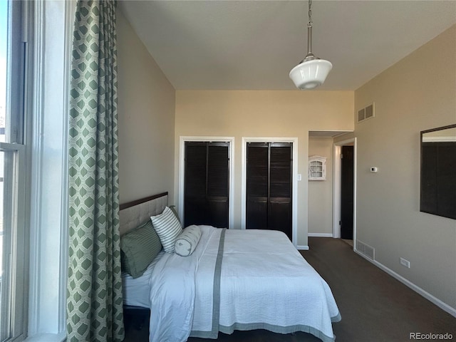 bedroom featuring dark colored carpet, visible vents, baseboards, and two closets