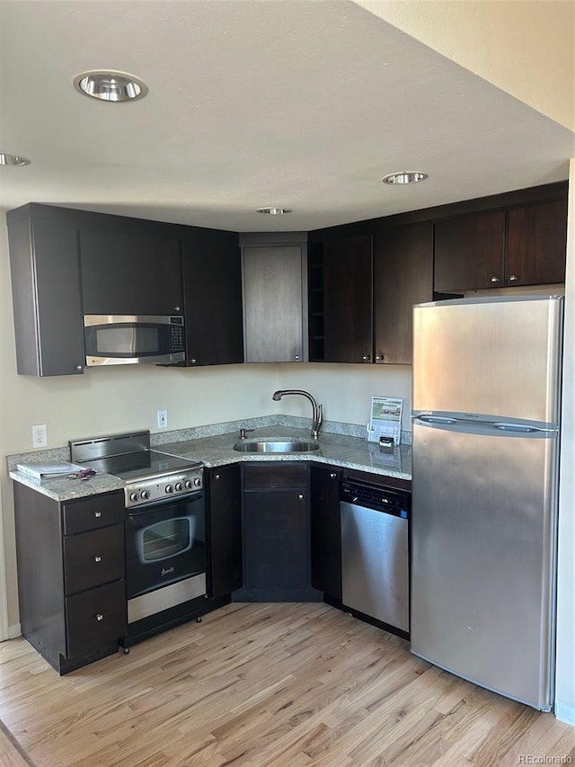 kitchen featuring stainless steel appliances, light wood finished floors, a sink, and light stone counters