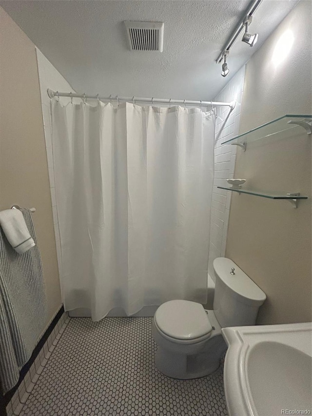 bathroom with a textured ceiling, toilet, visible vents, and curtained shower