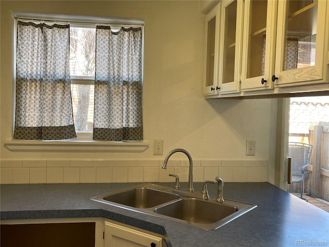 kitchen with dark countertops, glass insert cabinets, and a sink