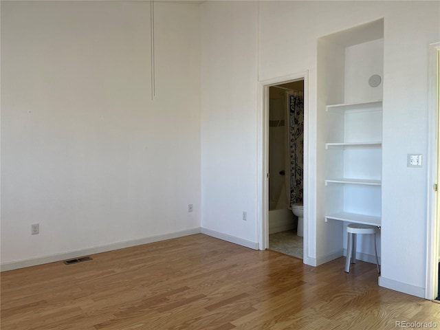 unfurnished bedroom featuring ensuite bathroom, baseboards, visible vents, and light wood finished floors