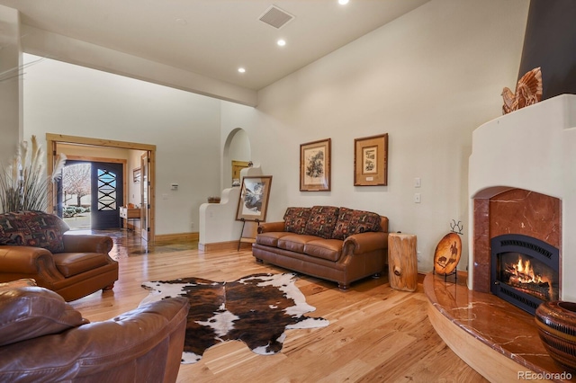 living room with light wood finished floors, a fireplace, a towering ceiling, and visible vents