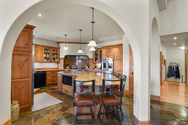 kitchen featuring brown cabinetry, a kitchen island with sink, stone tile floors, and black appliances