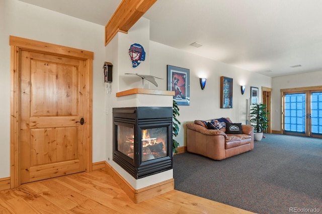 living area with wood finished floors, a multi sided fireplace, beam ceiling, and baseboards