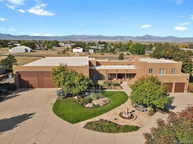 pueblo-style house featuring a garage, concrete driveway, a chimney, a mountain view, and stucco siding