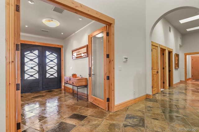 entryway with arched walkways, french doors, stone finish floor, and baseboards