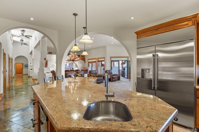 kitchen with a center island with sink, arched walkways, open floor plan, built in refrigerator, and a sink