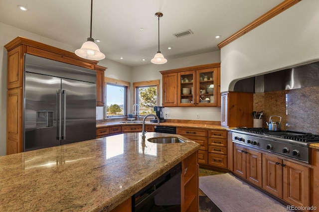 kitchen featuring brown cabinets, light stone counters, stainless steel appliances, and a sink