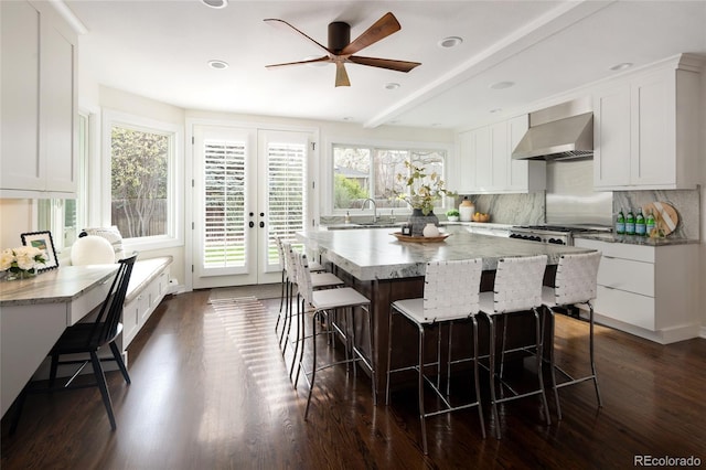 kitchen featuring a center island, a breakfast bar, white cabinetry, backsplash, and wall chimney range hood