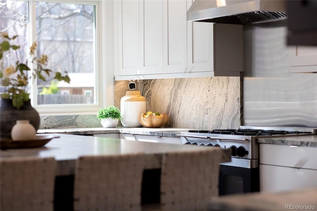 kitchen featuring stainless steel gas cooktop, tasteful backsplash, wall chimney range hood, light countertops, and white cabinets
