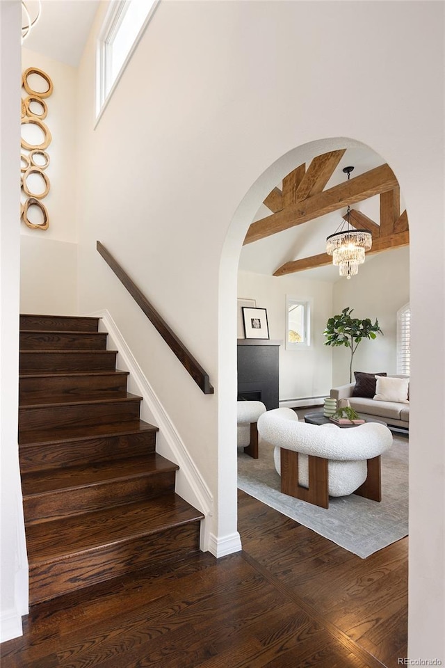 stairs with arched walkways, beamed ceiling, baseboards, and wood finished floors