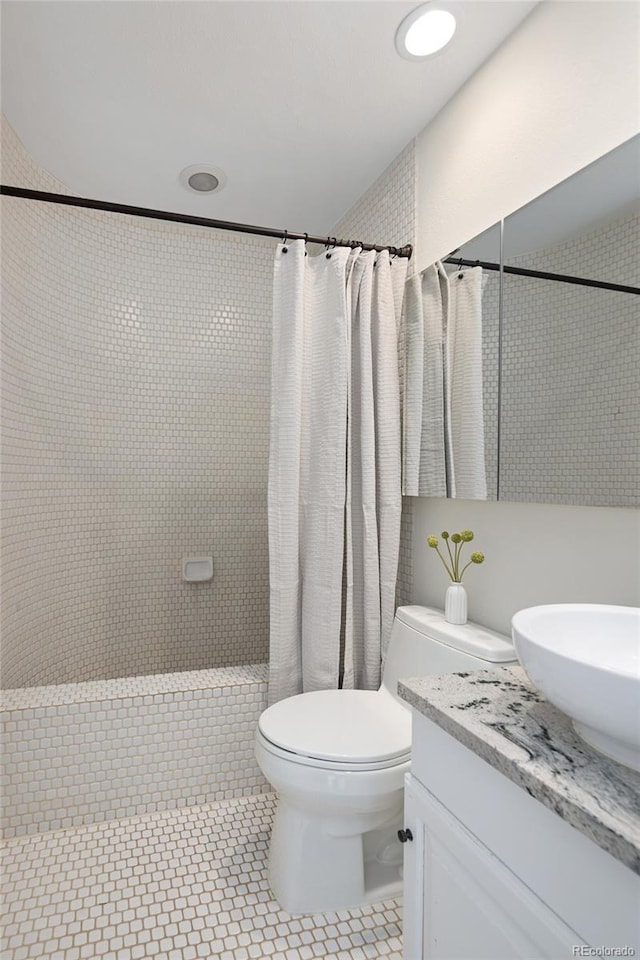 bathroom featuring toilet, tiled shower, vanity, and tile patterned flooring