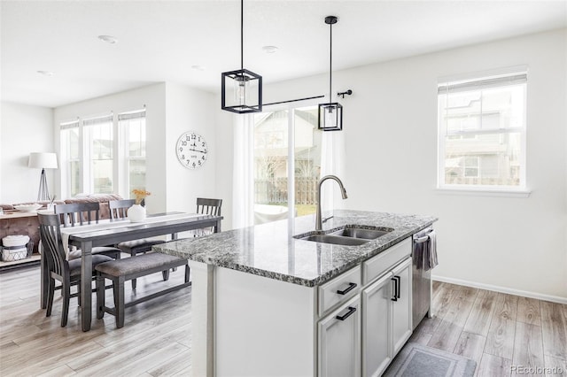 kitchen with stone countertops, sink, an island with sink, decorative light fixtures, and light hardwood / wood-style floors