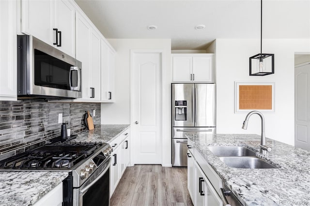 kitchen featuring pendant lighting, sink, light stone countertops, white cabinetry, and stainless steel appliances