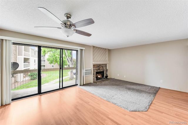 4896 S Dudley St Unit 4-7, Littleton, CO 80123 - unfurnished living room with a ceiling fan, wood finished floors, a stone fireplace, a textured ceiling, and a wall unit AC