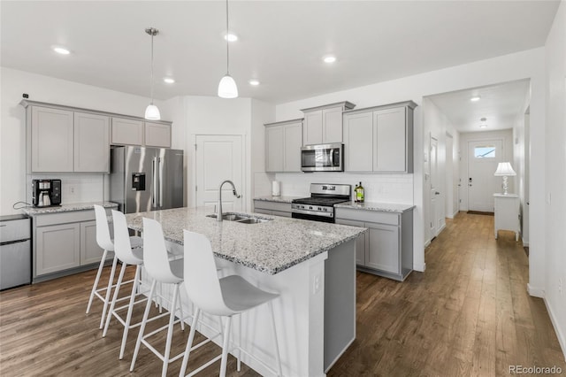 kitchen featuring sink, light stone counters, pendant lighting, stainless steel appliances, and a kitchen island with sink