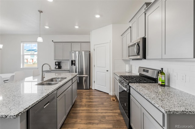 kitchen with sink, light stone counters, decorative light fixtures, a center island with sink, and stainless steel appliances