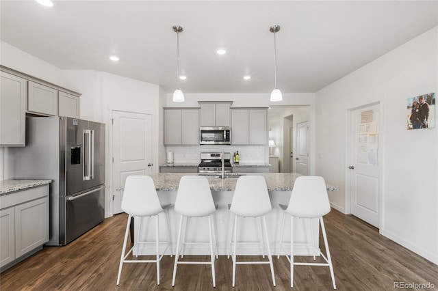 kitchen featuring a kitchen island with sink, hanging light fixtures, stainless steel appliances, and light stone countertops